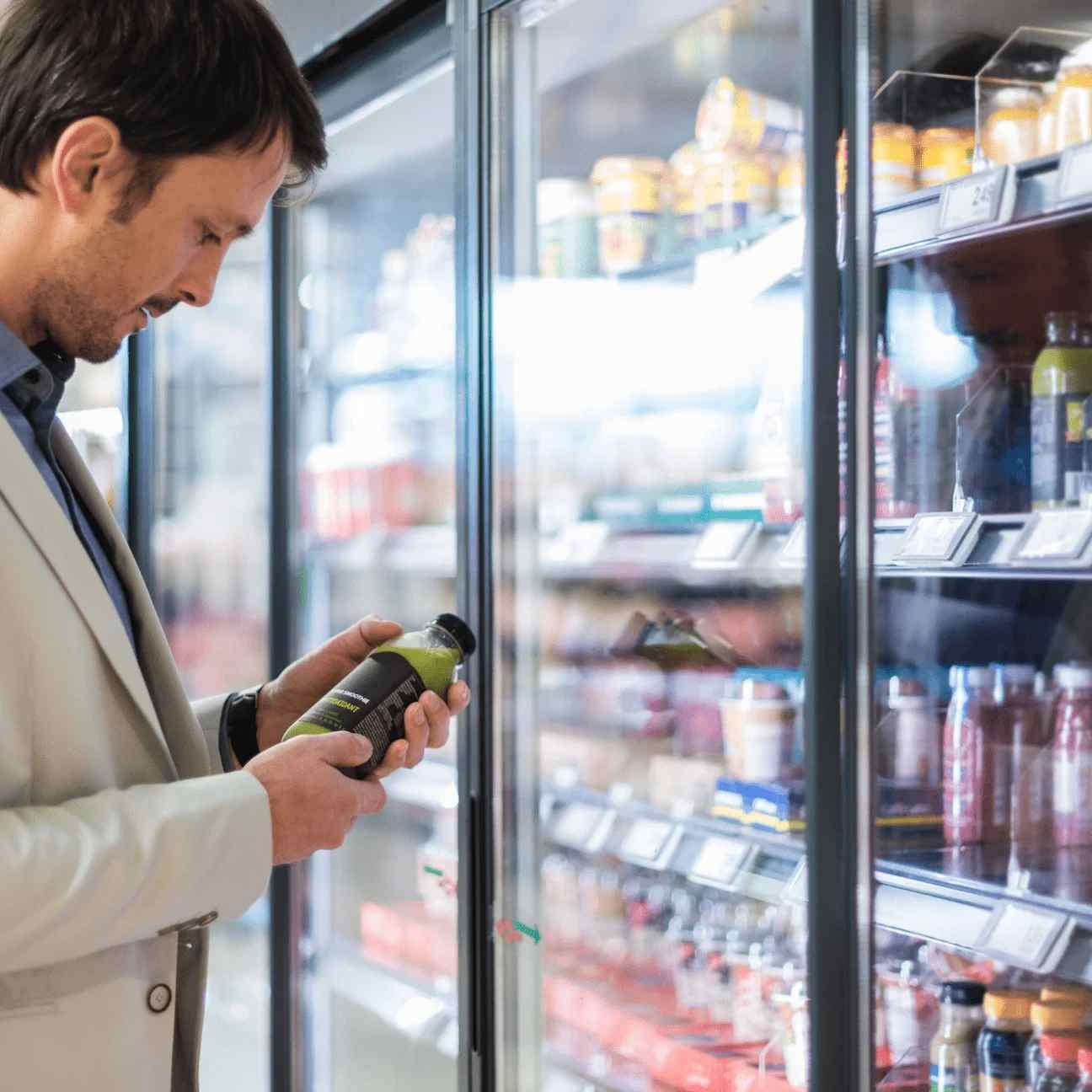 A person is stand infront of a refrigerator with holding a cold drink