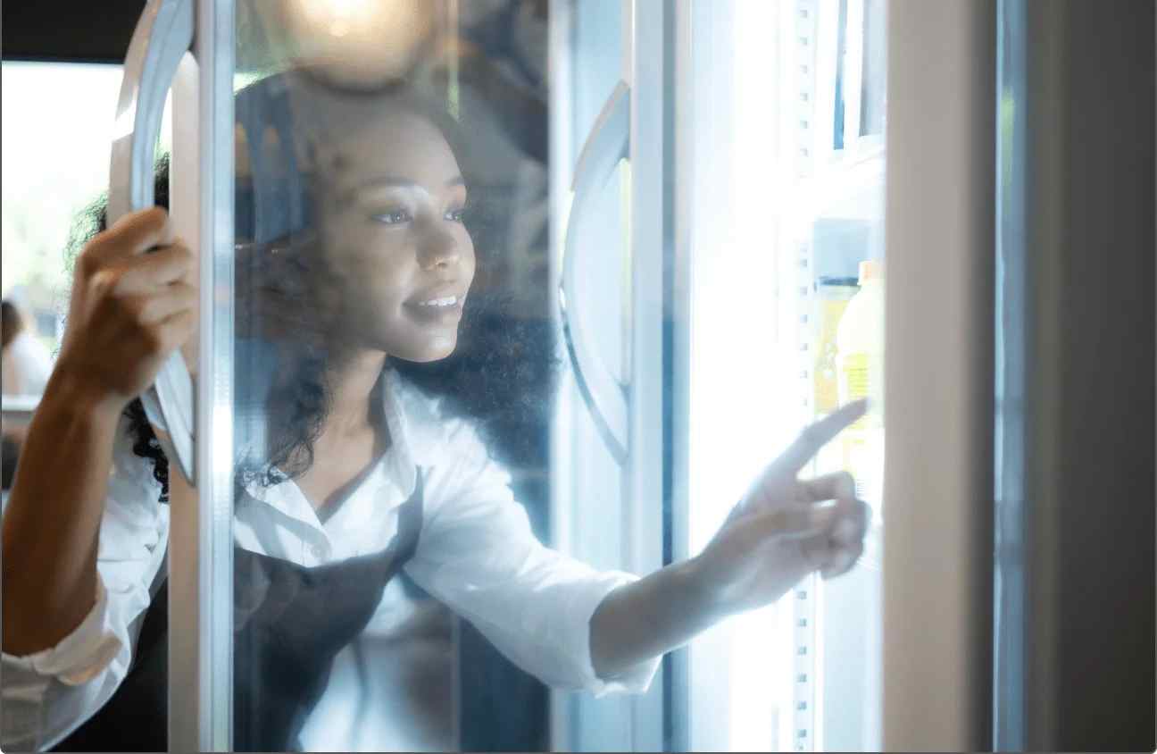 A female chef has opened door of refrigerator and check or adjust temperature