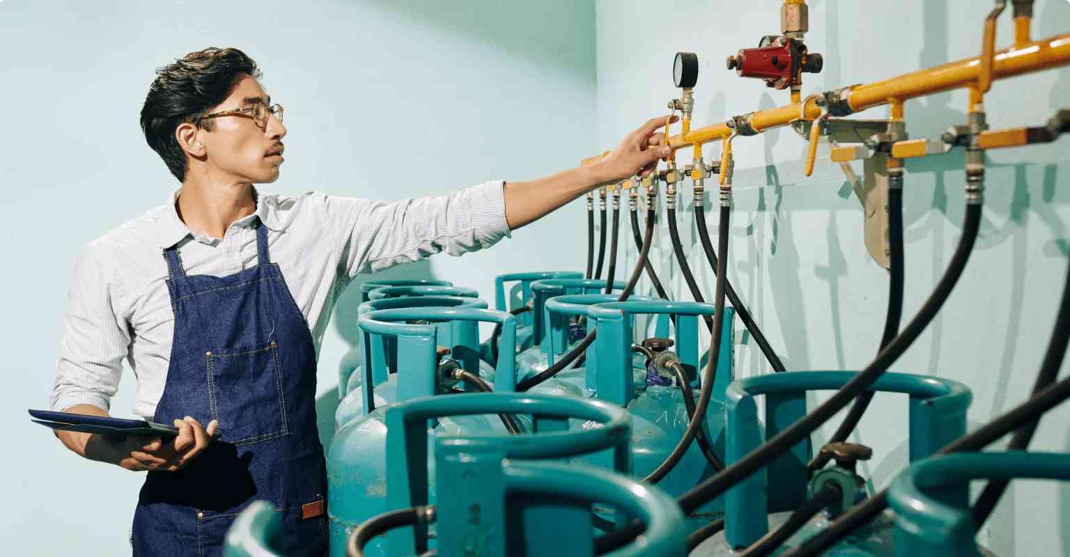 A worker holds tablet in right hand and check cylinder pipelines with his left hand